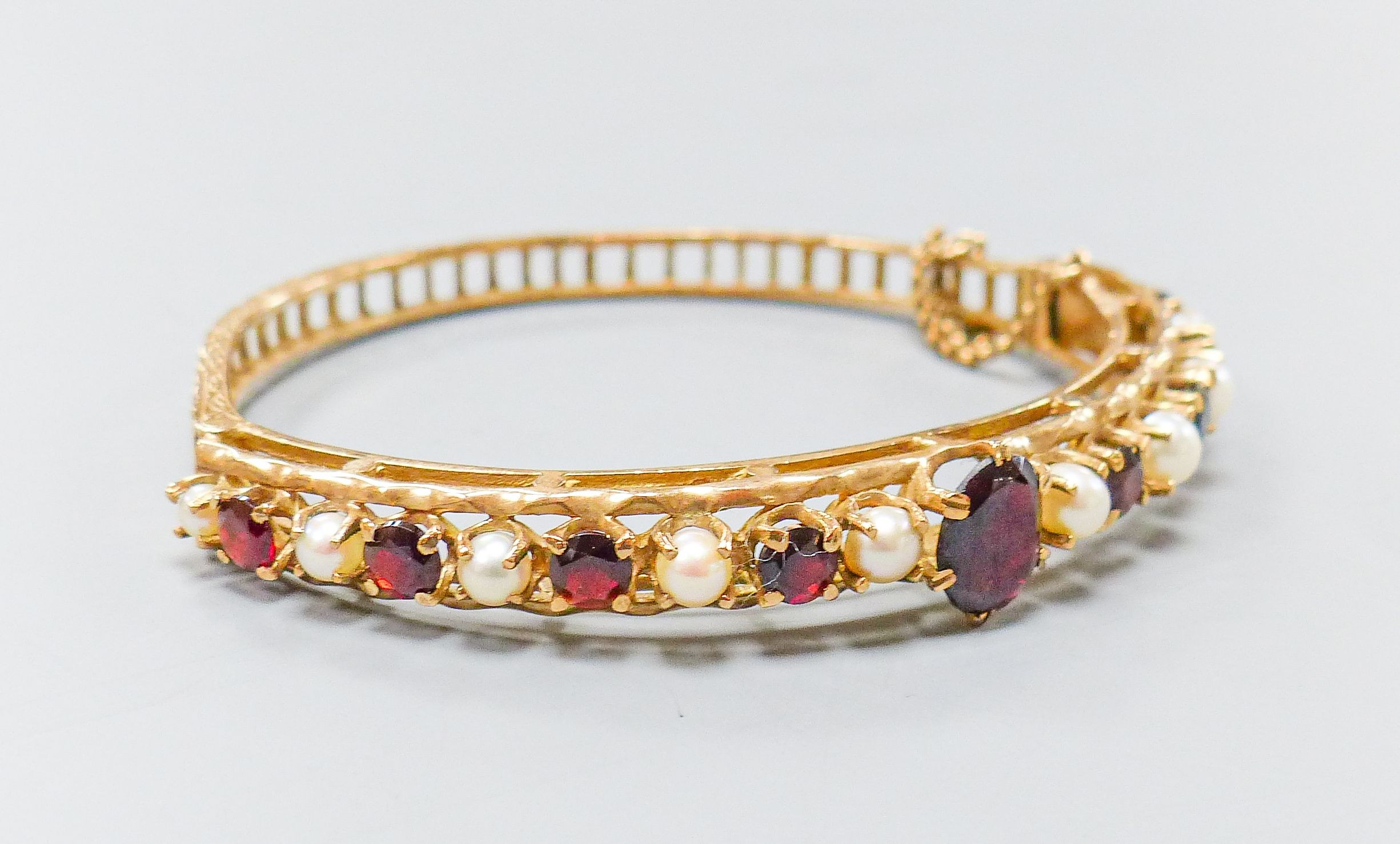 A 9ct gold, garnet and cultured pearl set hinged bracelet, gross weight 16.1 grams.